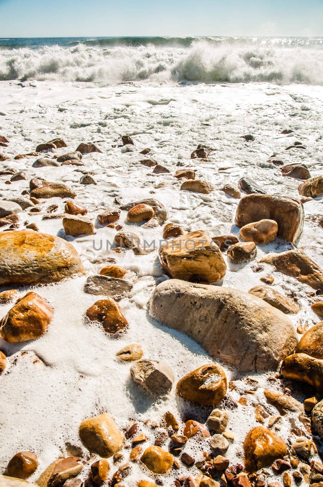 Waves crashing on a rocky beach as the tide is coming in, leaving white wake behind as the water resides.
