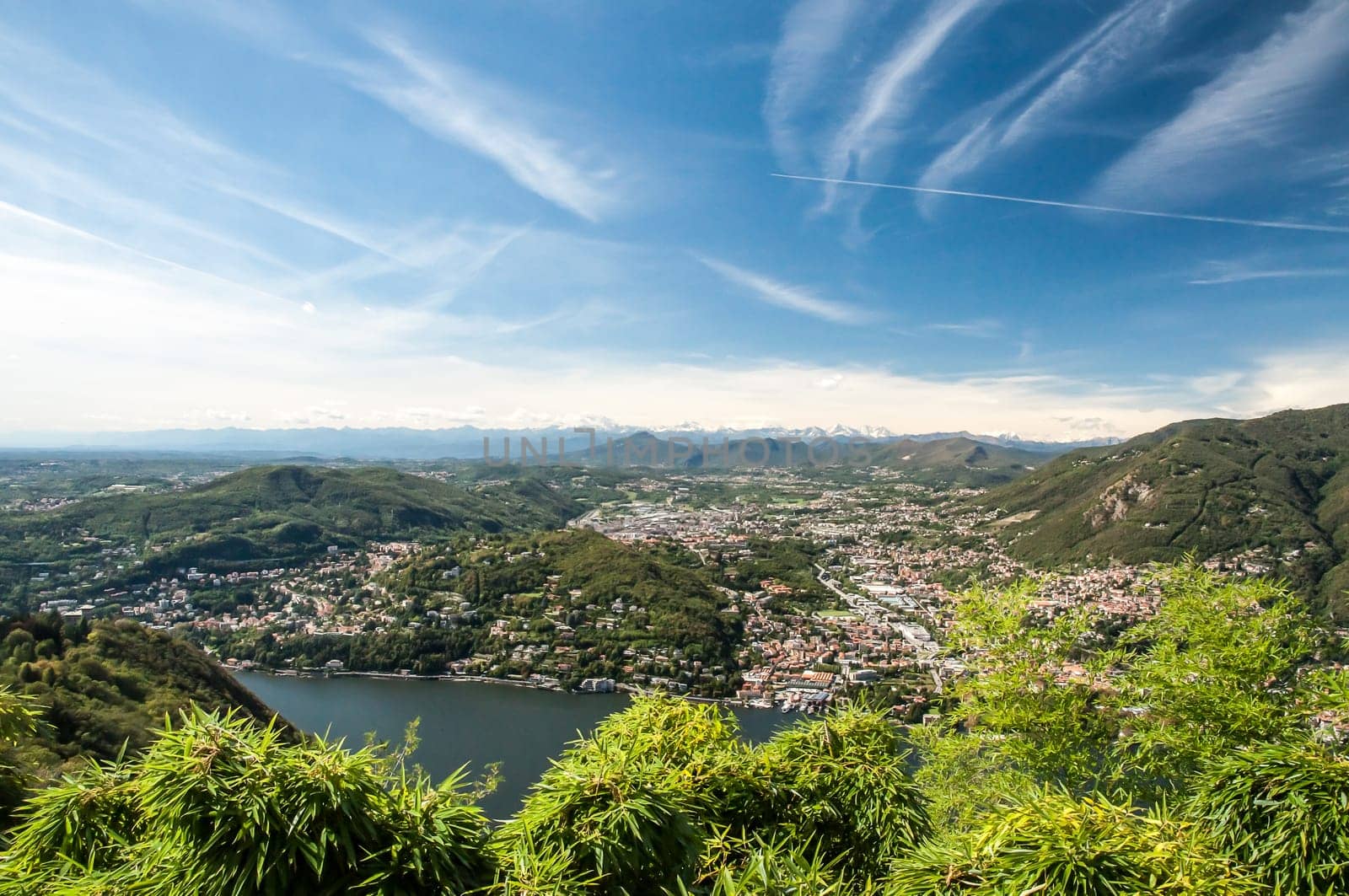 A view of Lake Como, the Town called Como and the Alps in the far distance with blue skys and white clouds.