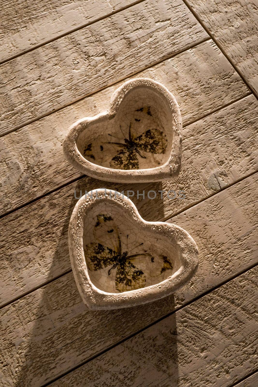 Two heart decorations on a white whashed wooden table in low directional light of the late afternoon.