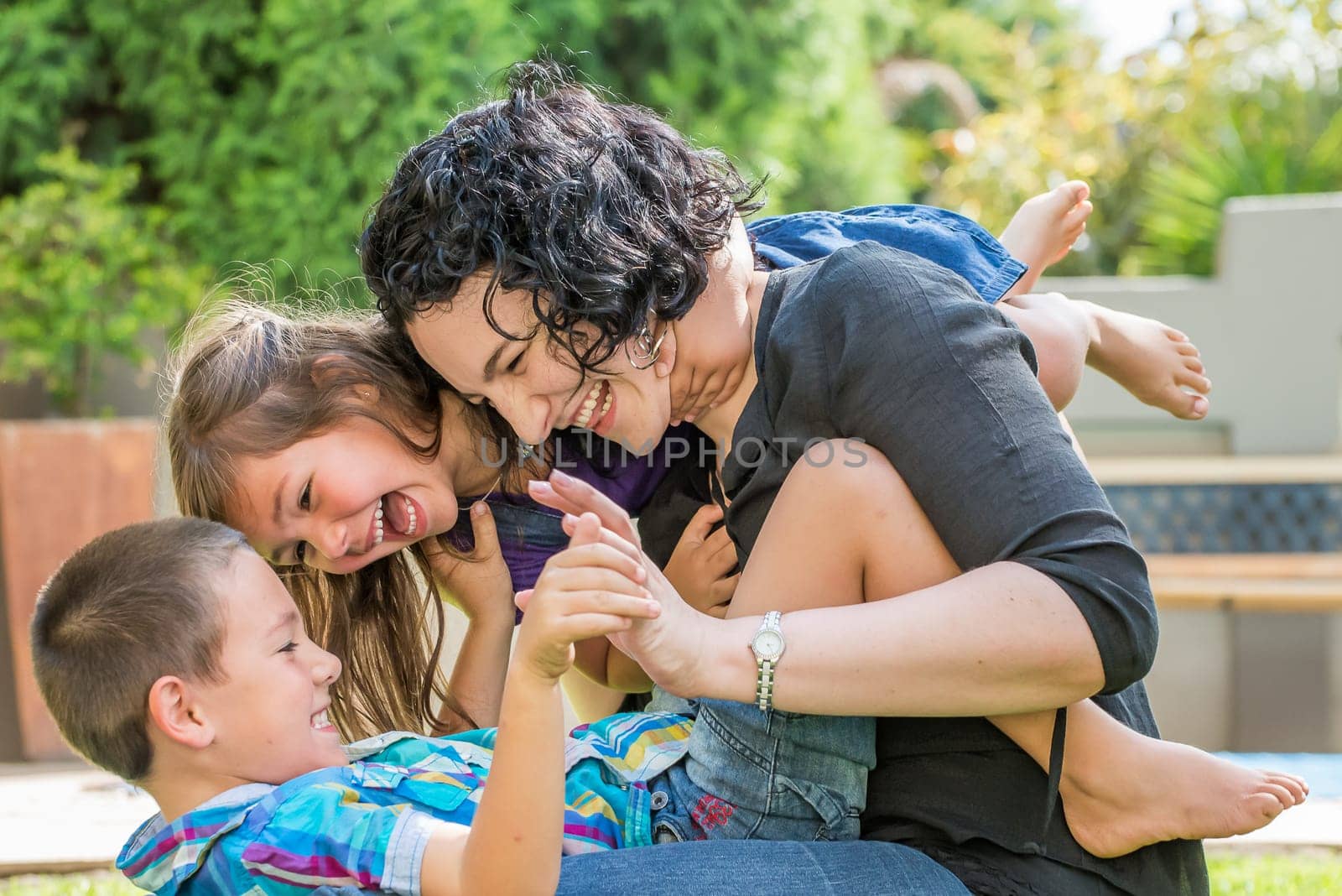 Young mother, son and daughter playing outside on the lawn in sunny weather, having fun, laughing with joy.
