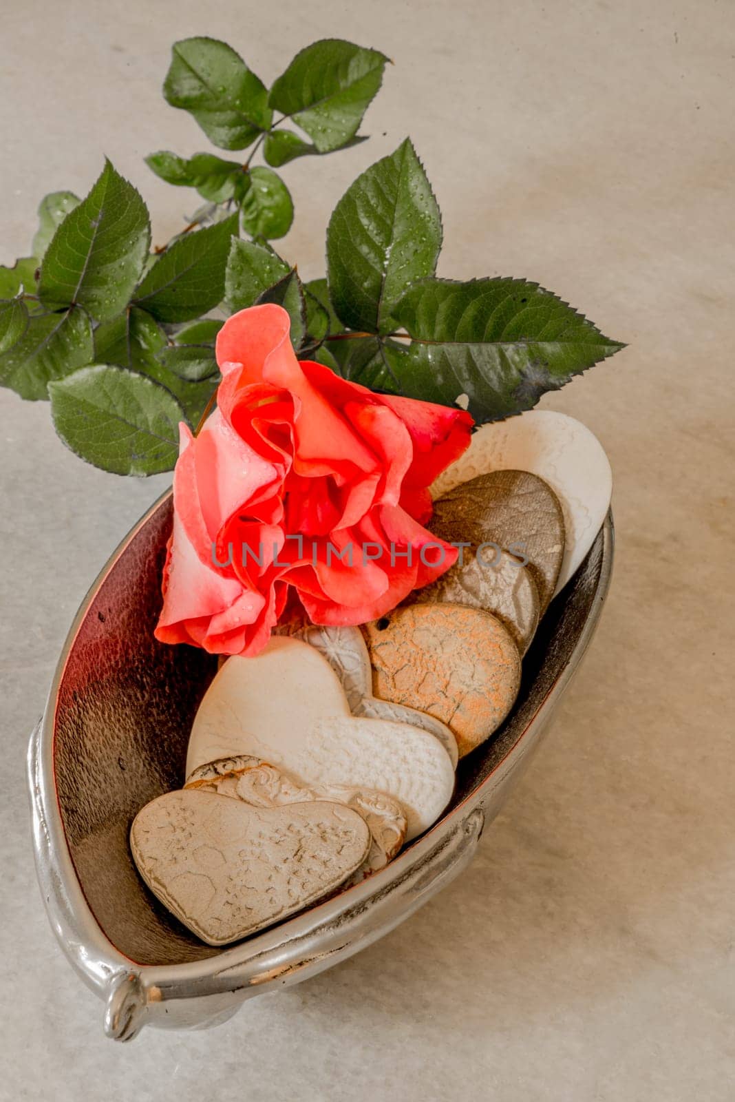 Hearts made from porcelain with the imprints of doylies placed inside a silver bowl with a red rose on top.