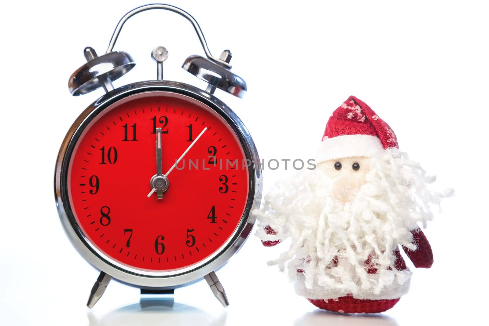 Santa Claus or Father Frost and vintage alarm clock with red dial on white background with reflection. Showing time twelve midnight