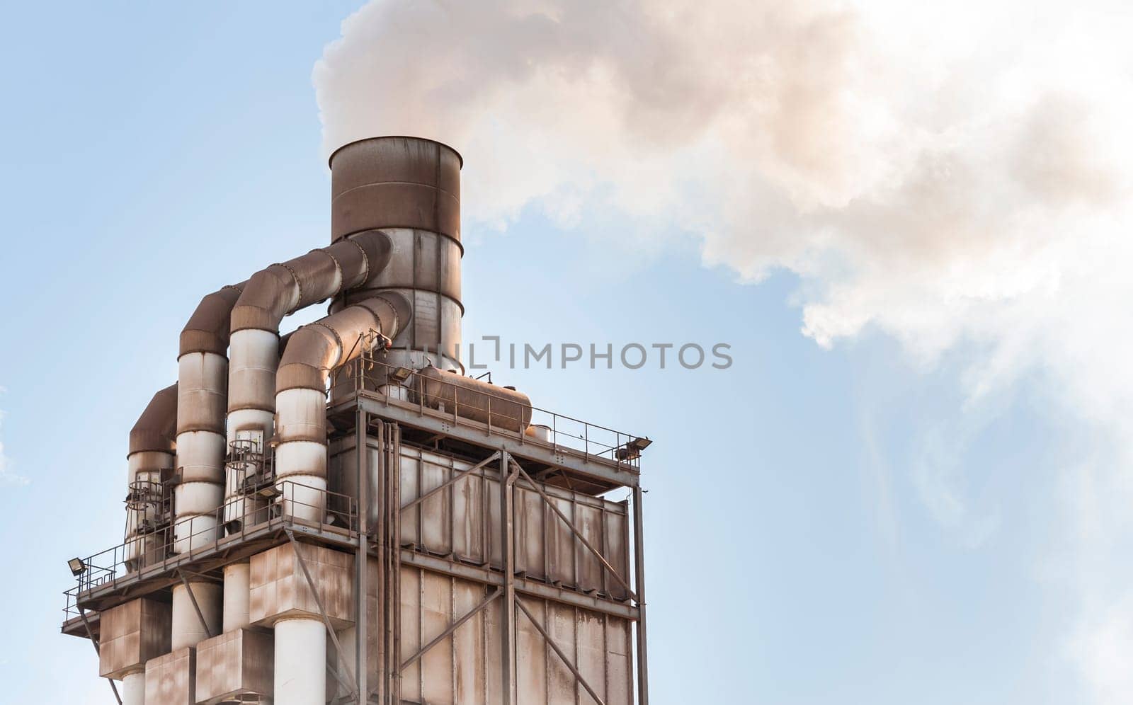 Old smokestack that emits white smoke in the clear blue sky.