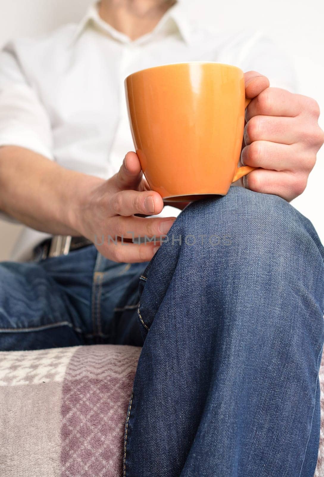 Man resting on a sofa and holding a cup of coffee