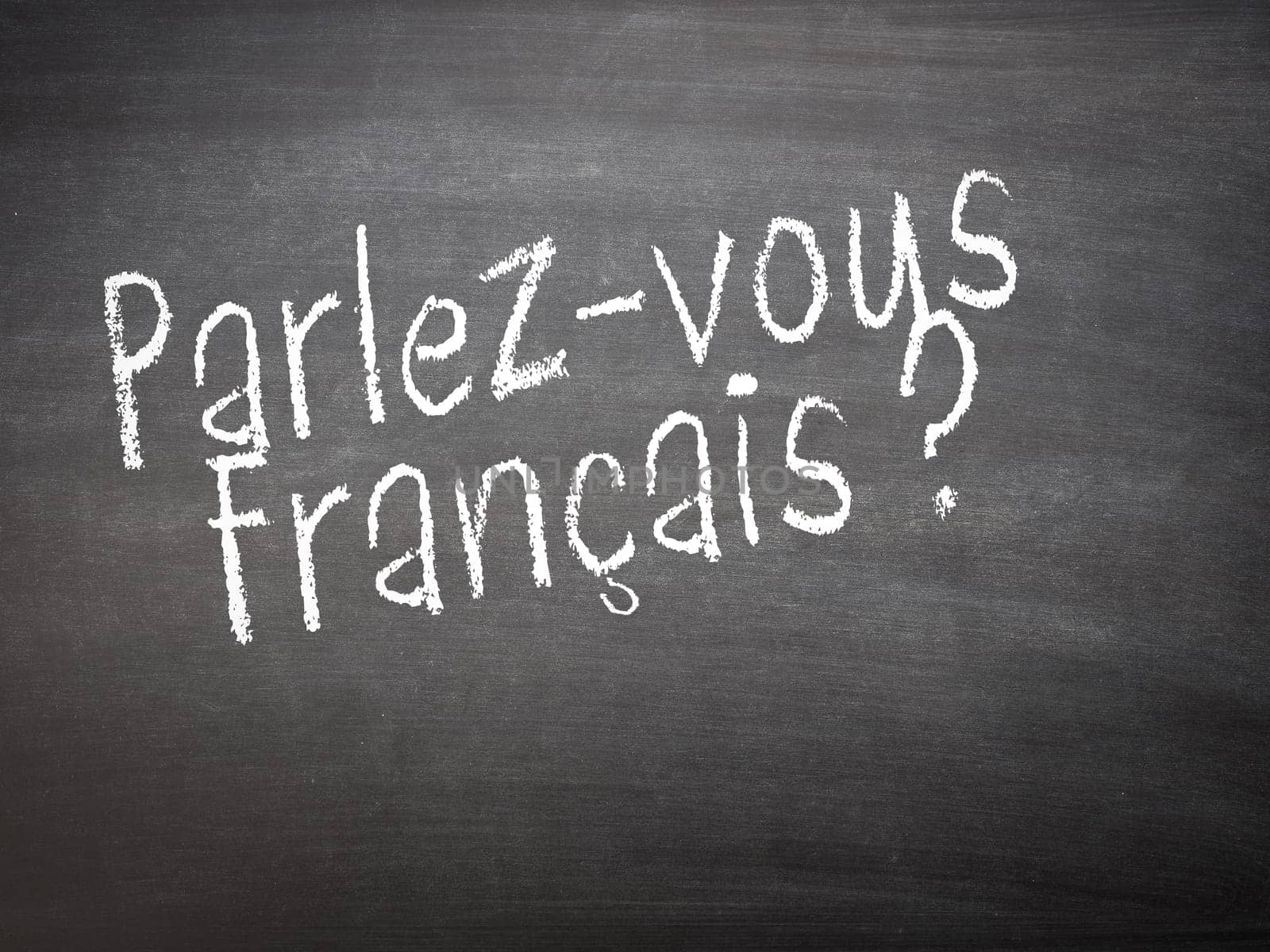 Learning language - French. Learning French language concept of teacher or student writing parlez-vous francais (do you speak French) on blackboard / chalkboard.