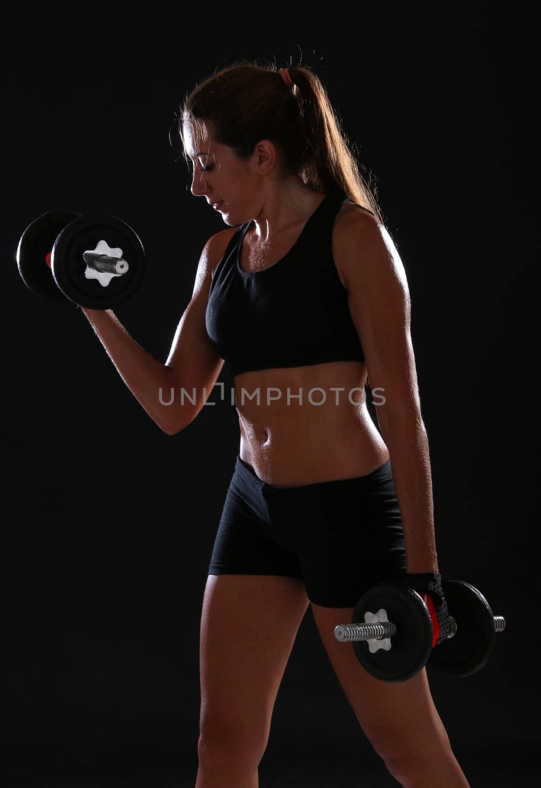 Young woman doing exercise with dumbbells, over black