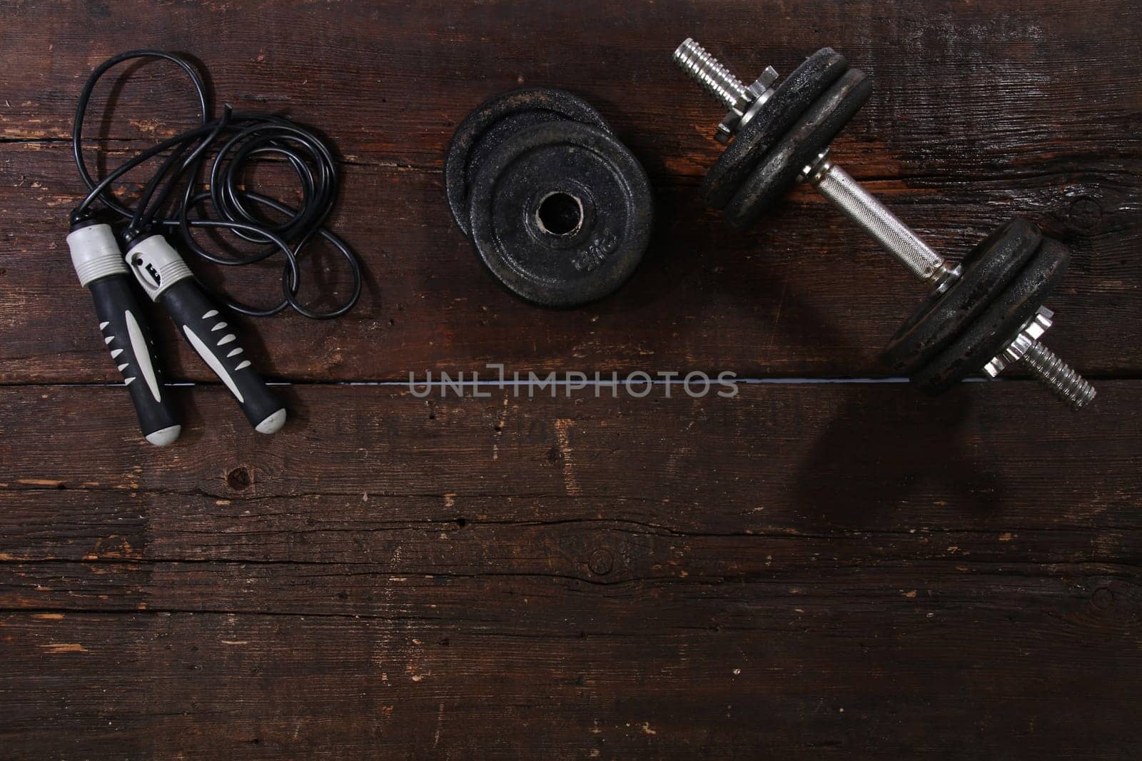 Dumbbell and a skipping rope on a rusty wooden floor