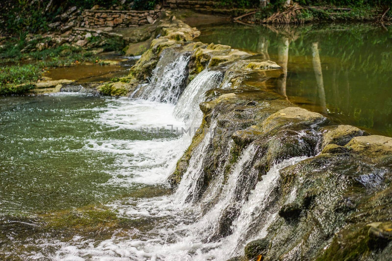 landscape with small waterfall by the lake on a summer day and green moss on the stones