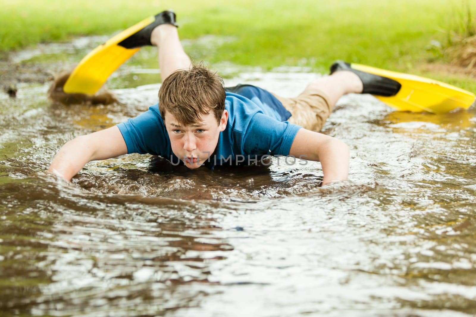 Serious male teenager in diving fins trying to swim in large shallow backyard puddle