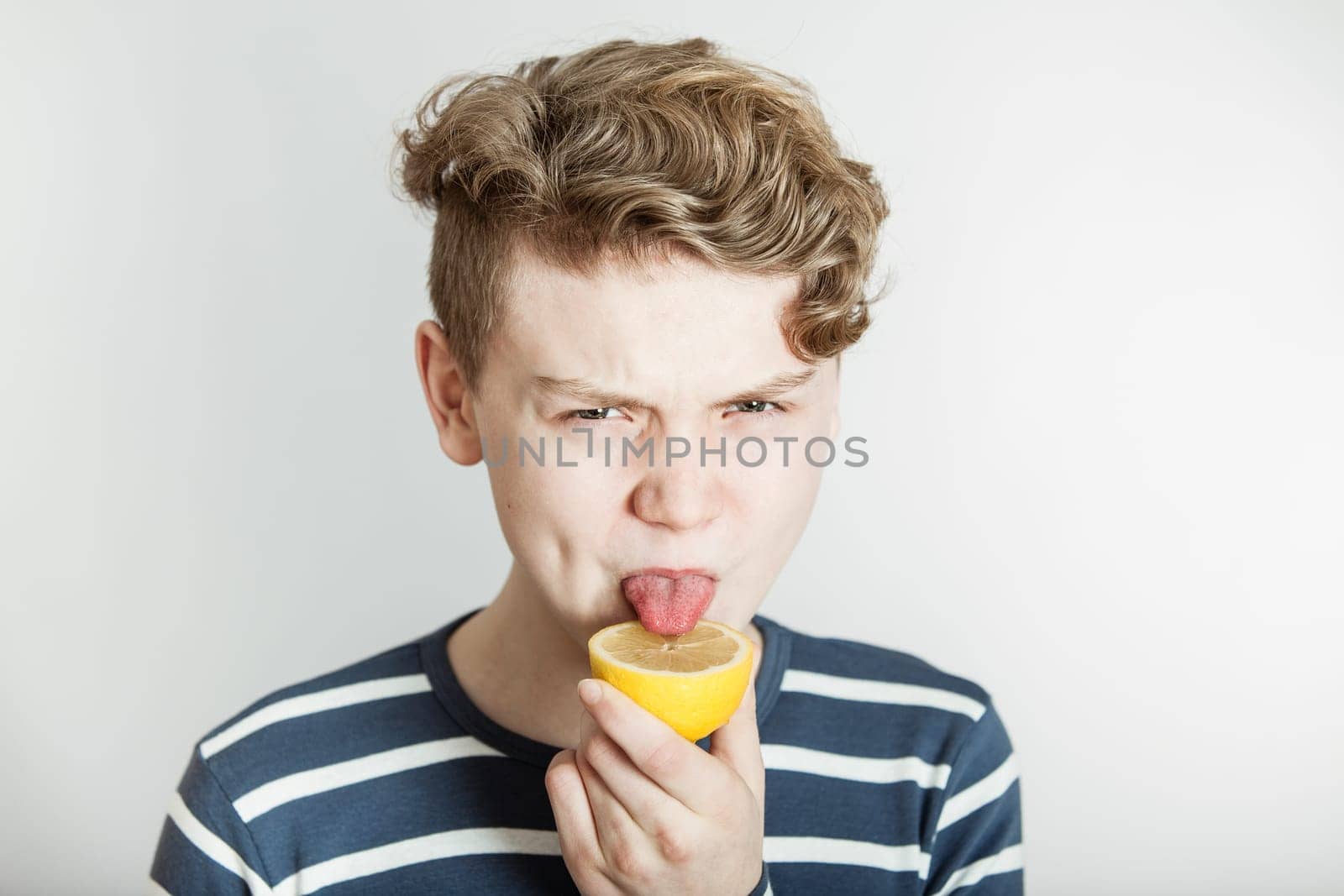 Head and Shoulders of Boy with Wavy Blond Hair Licking Sliced Lemon in Studio with White Background and Copy Space - Humorous Nutrition Concept Image