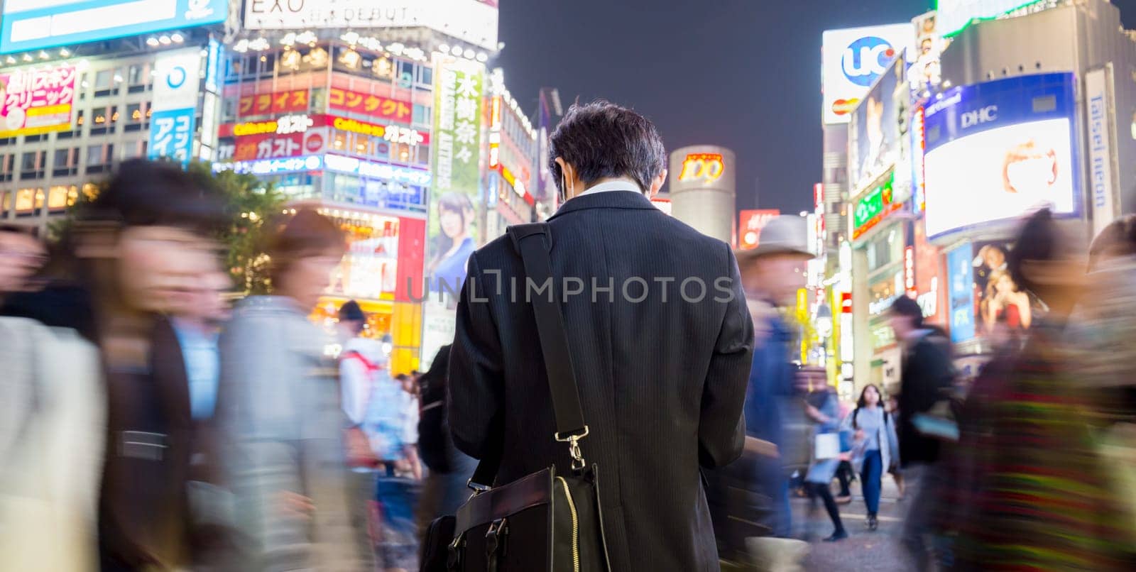 Solitary japanese corporative businessman in suit, after work, waiting in crowd on Shibuya crossing, famous shopping and entertainment district of Tokyo, Japan.