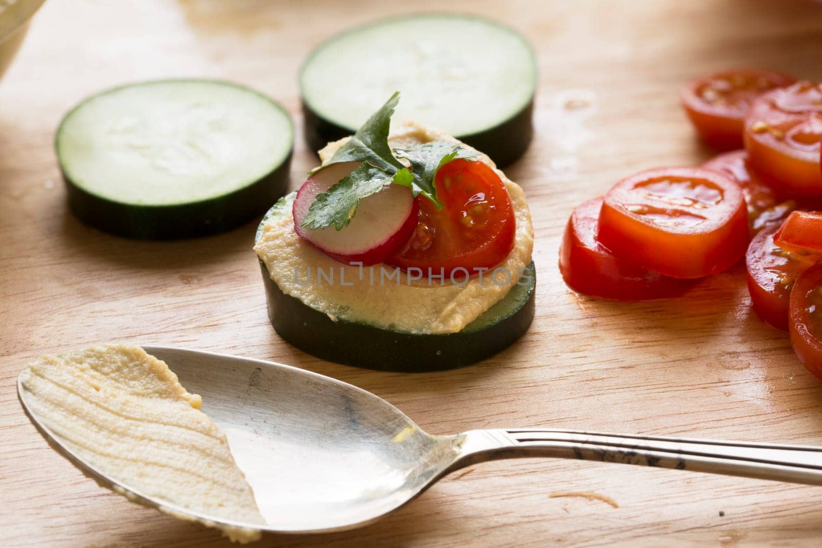 Healthy cucumber hummus bites with tomato, radish and cilantro on cutting board with spoon.