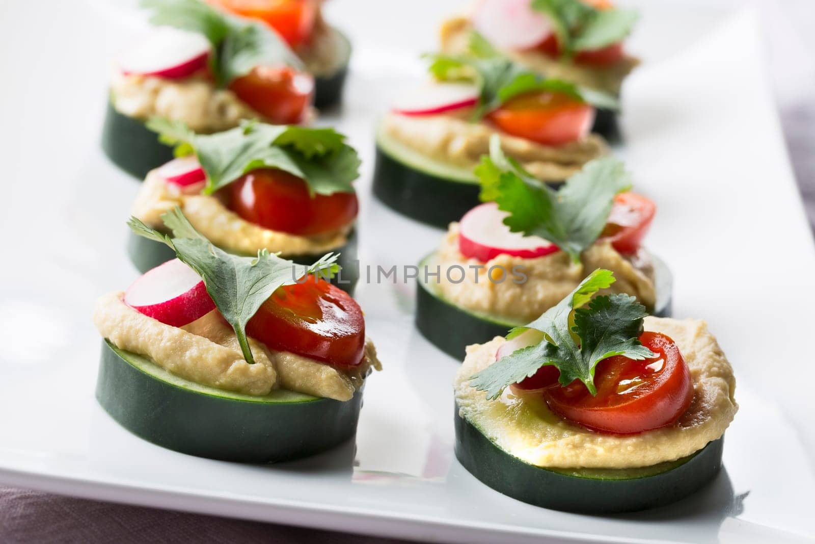 Healthy cucumber hummus bites with tomato, radish and cilantro.
