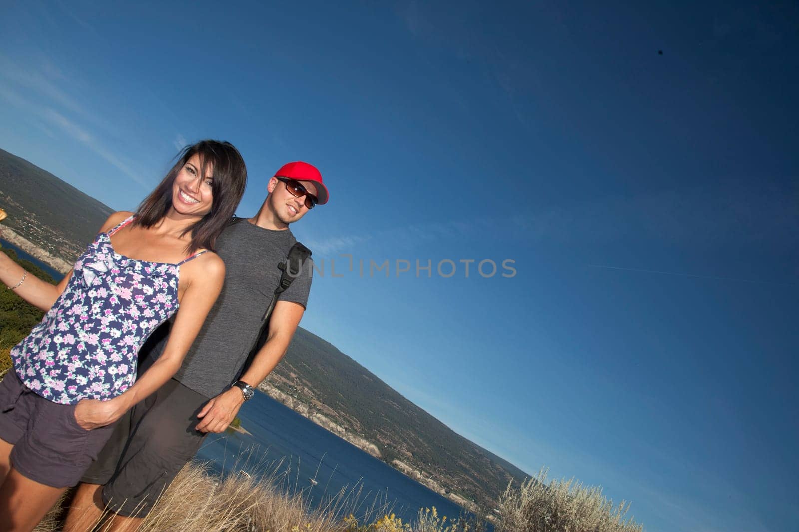 Outdoor photo of young, attractive couple hiking with mountains and lake in background.