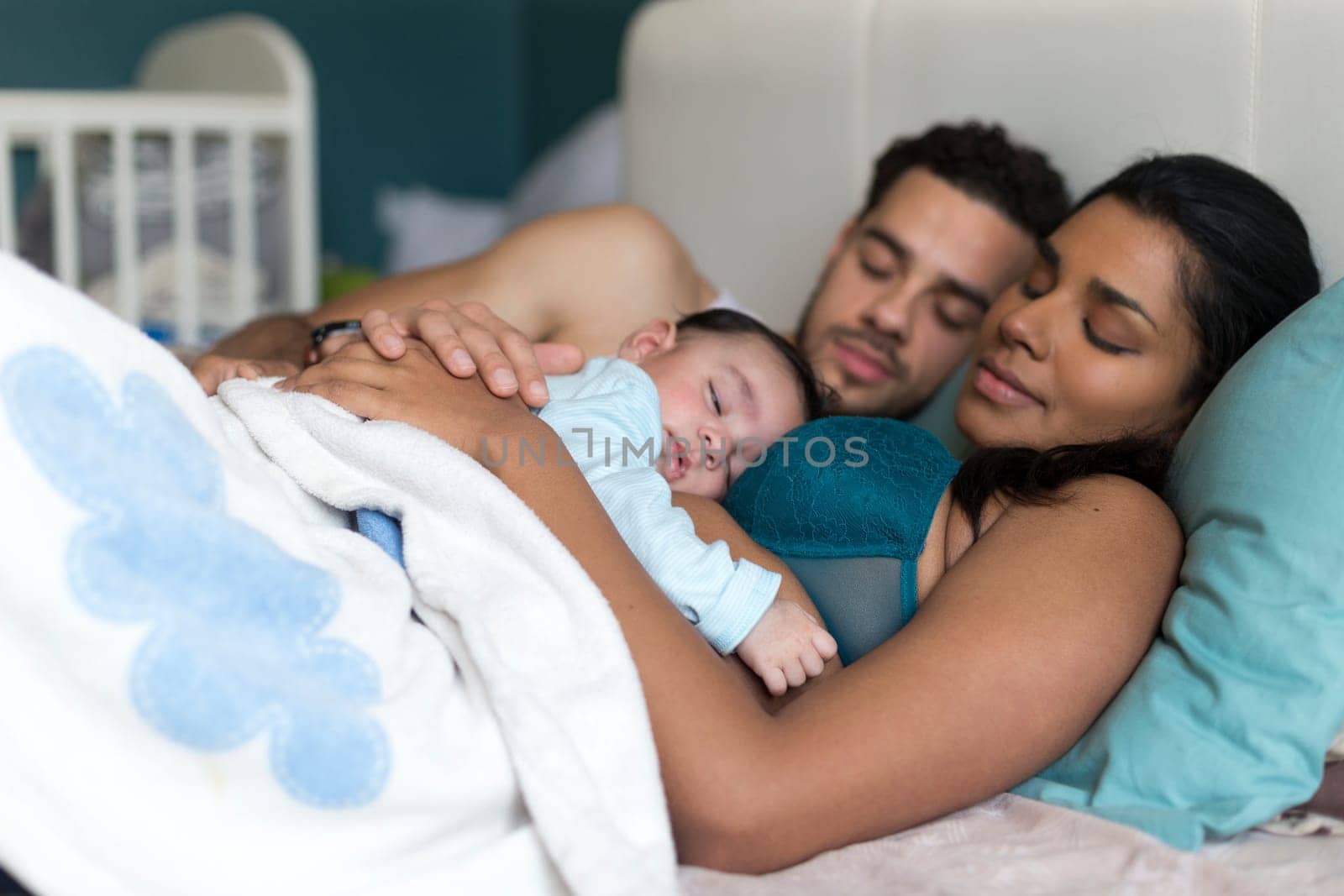 Young couple asleep in bed with their baby son sleeping on his mothers chest.