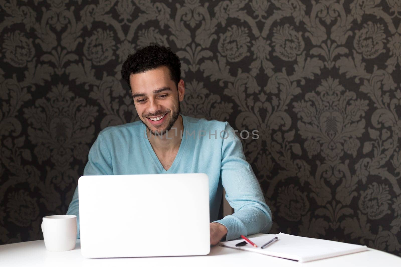 Young man using a laptop at home. He is looking at the screen and smiling.