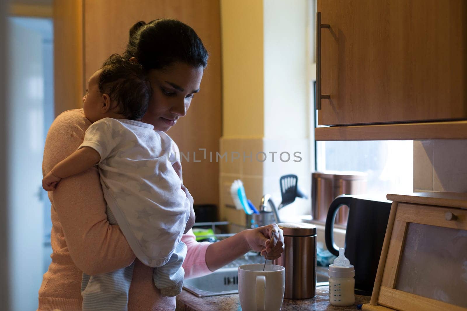 Young mother making a cup of tea with her baby son on her shoulder