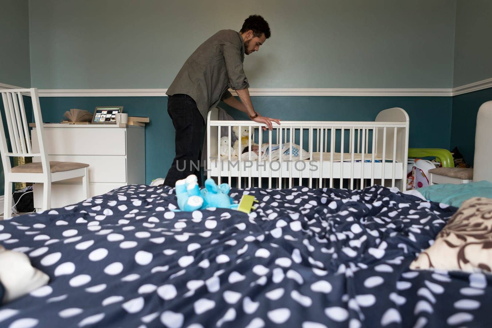 Young father checking on his baby son, who is asleep in a copt in the bedroom.