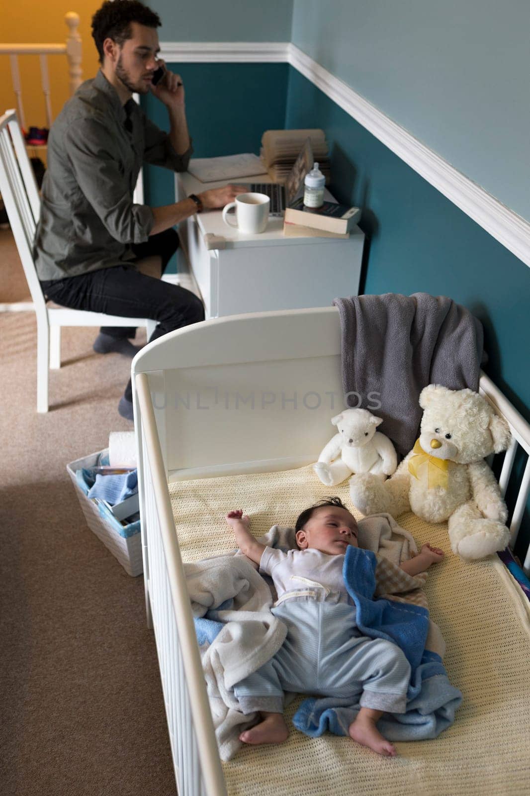Young father working from home whilst his baby son is sleeping in his cot.