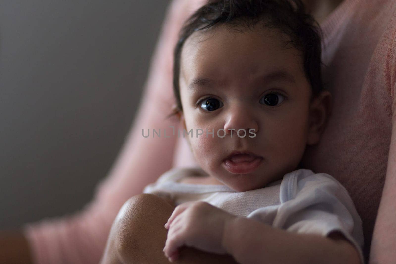 Portrait of a 3 month old baby boy. He is being held by his mother and looking at the camera.
