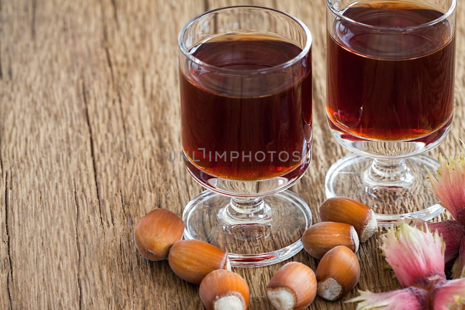 Homemade Hazelnut liqueur in two glasses and hazelnuts of an old rustic wooden table