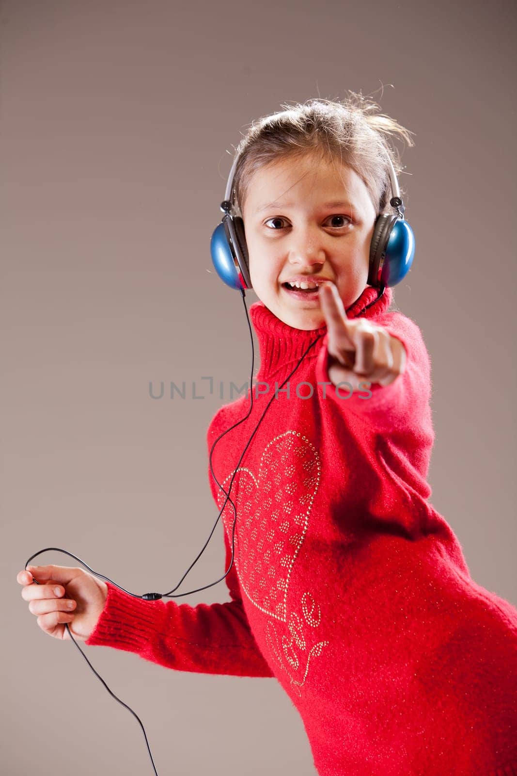 Little girl dancing and pointing her finger to you while listening to the music in her blue headphones and dancing