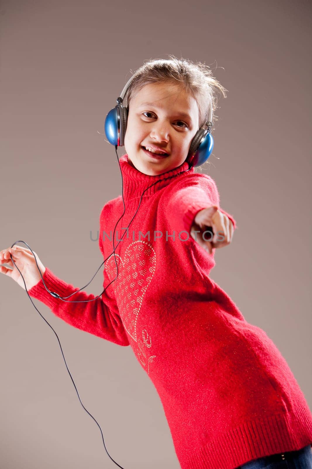 Little girl dancing and pointing her finger to you while listening to the music in her blue headphones and dancing