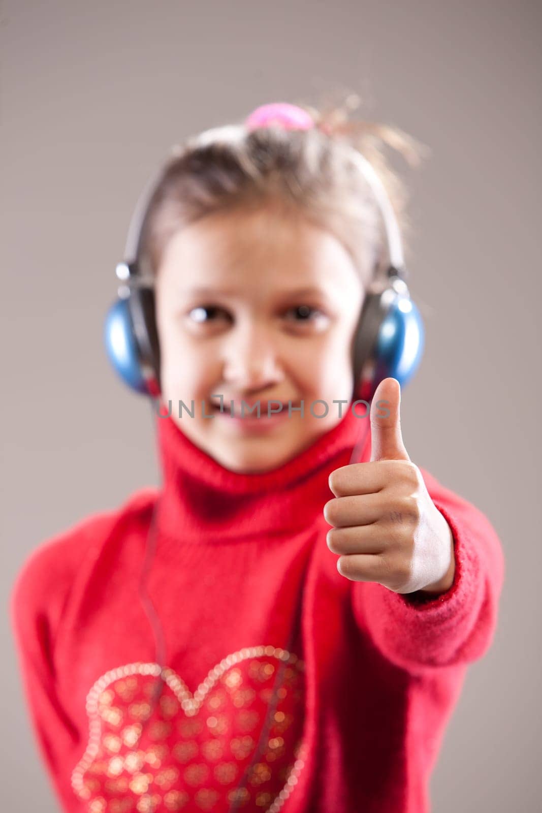 Little girl listening to the music inher blue headphones and showing her thumb up (IN FOCUS) the face is out of focus