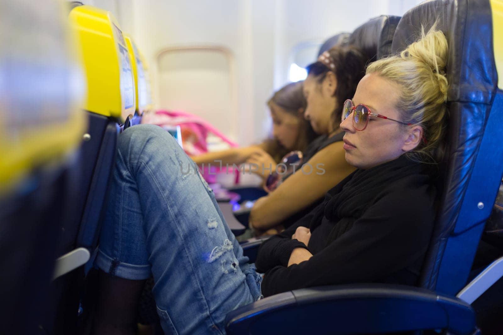People flying by plane. Interior of airplane with passengers sleeping on seats. Tired woman napping on uncomfortable seat on airplane. Commercial transportation by planes.