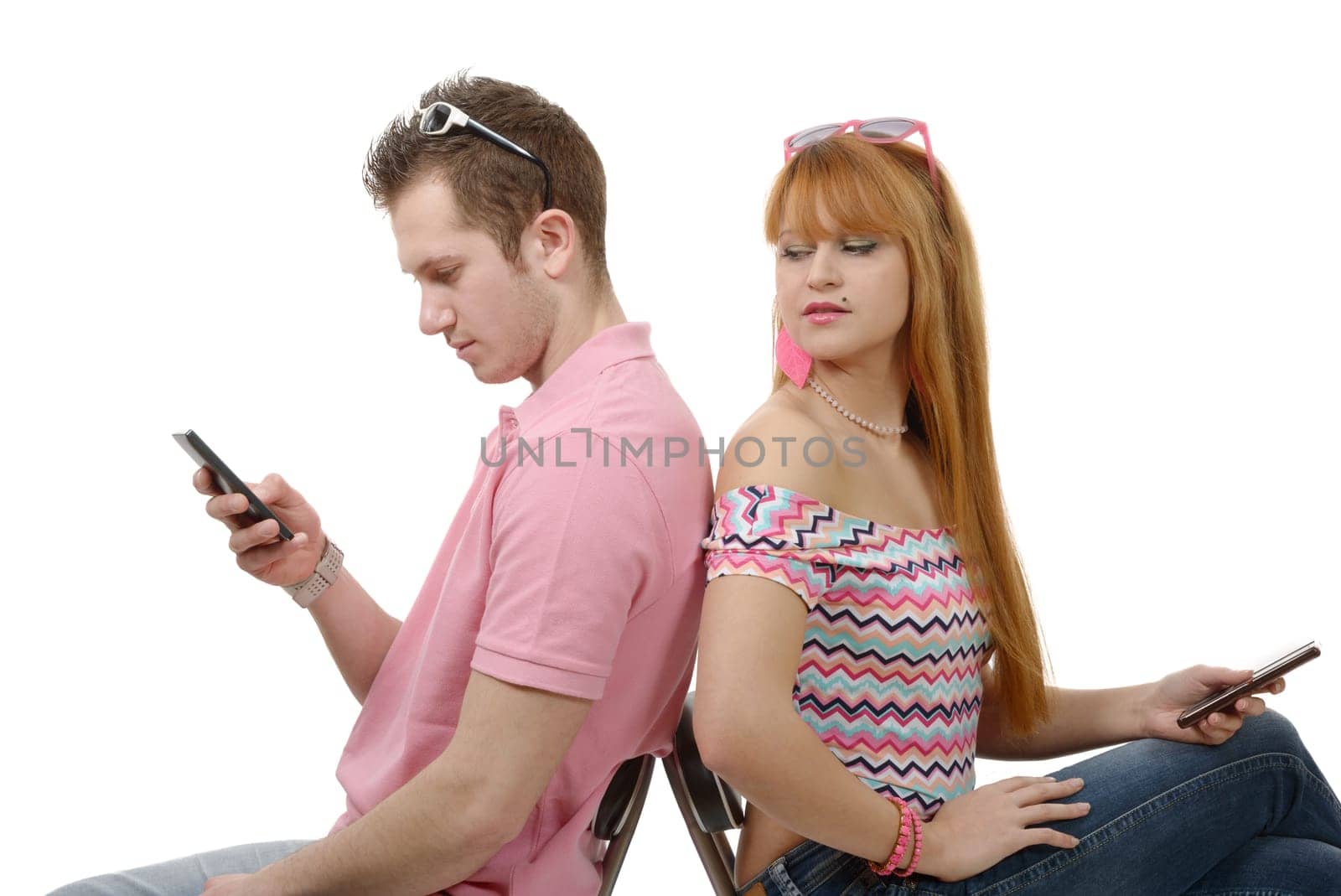 a young couple talking on mobile phones sitting back to back.
