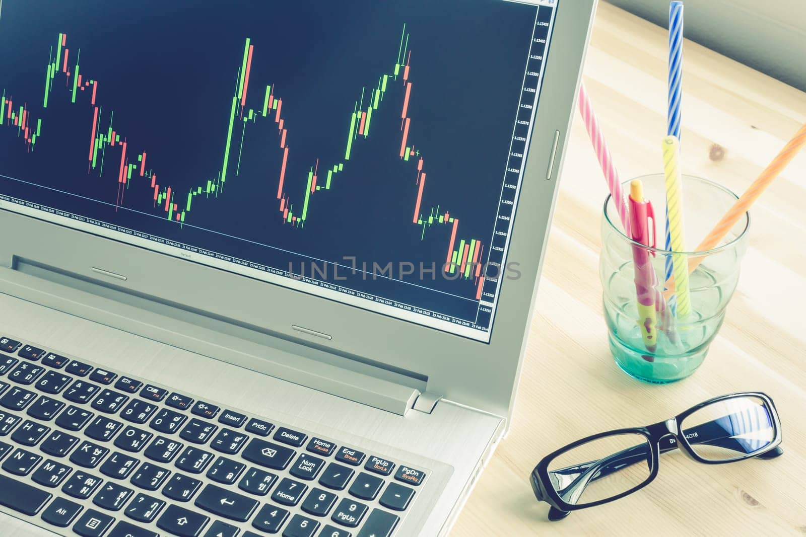 Forex graph or stock graph in laptop screen on wood table and pen and black glasses on Blue Vintage Style