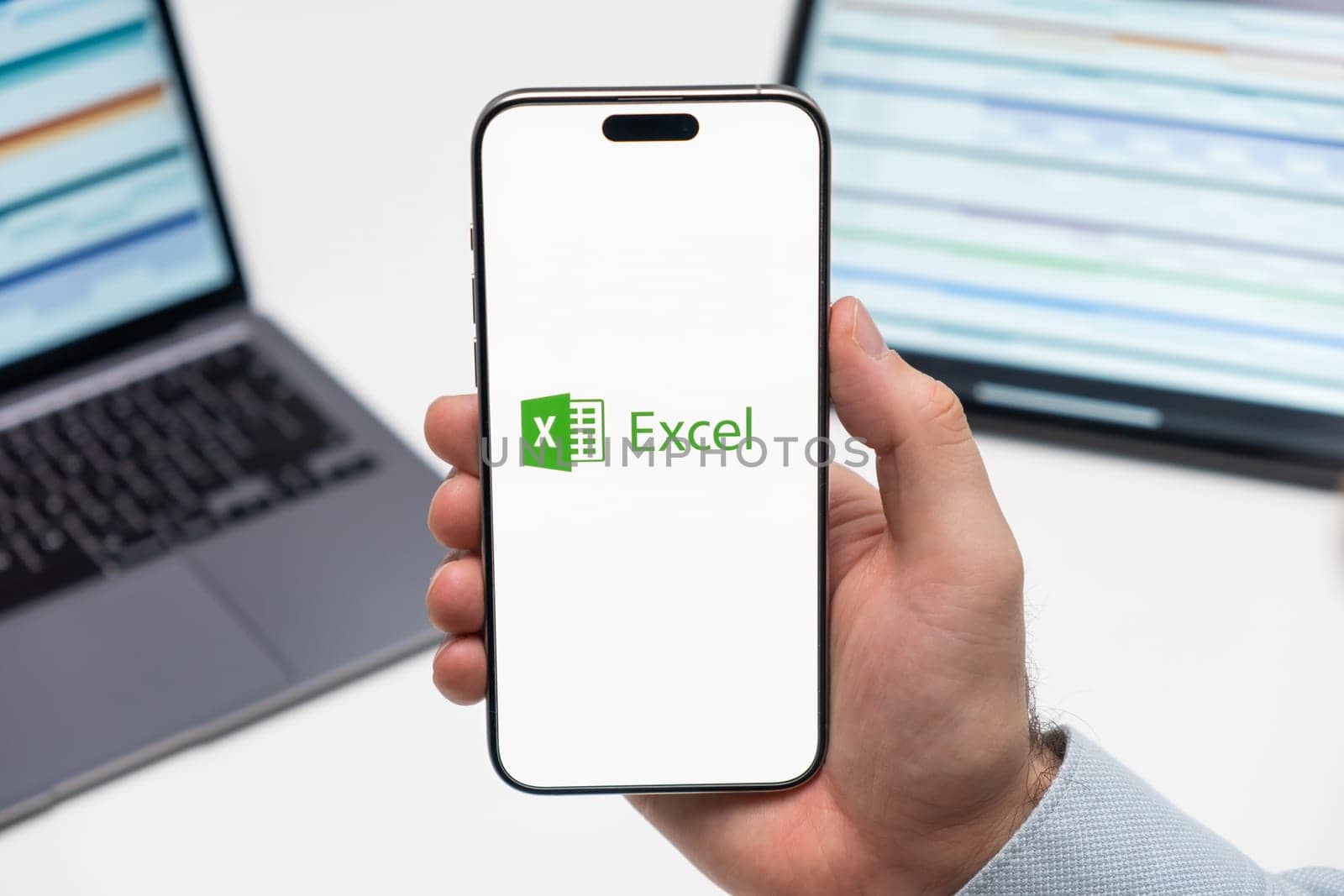 PRAGUE, CZECHIA - JULY, 2024: Excel logo on the screen of smartphone in mans hand and laptop on the background