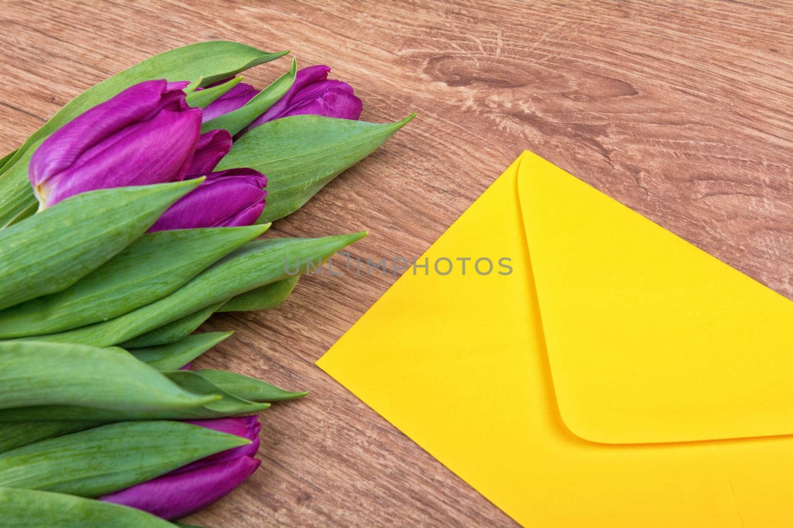 Yellow envelope with purple tulips on a wooden background