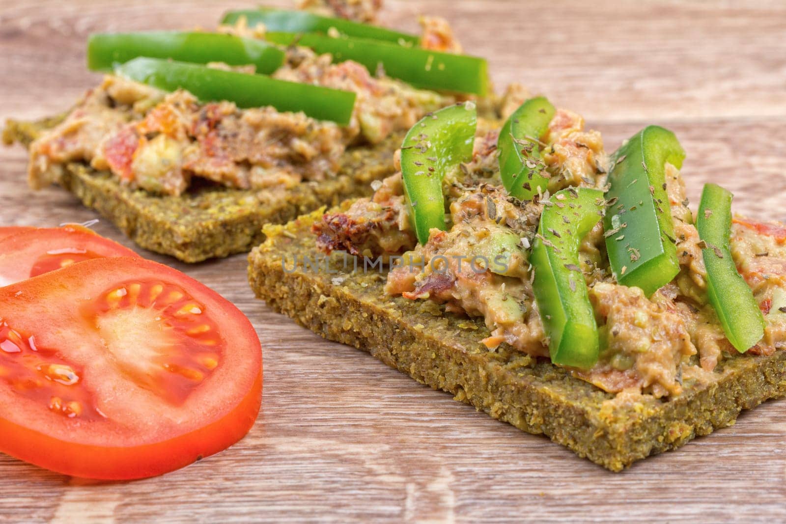 Raw bread with a spread decorated with green pepper and tomatoes