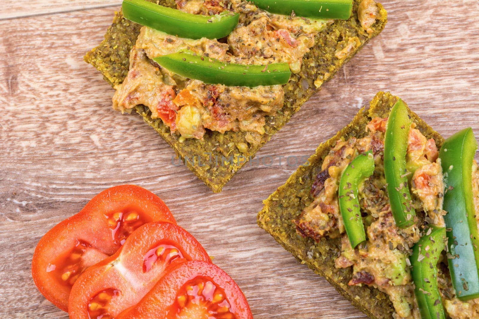 Raw bread with a spread decorated with green pepper and tomatoes