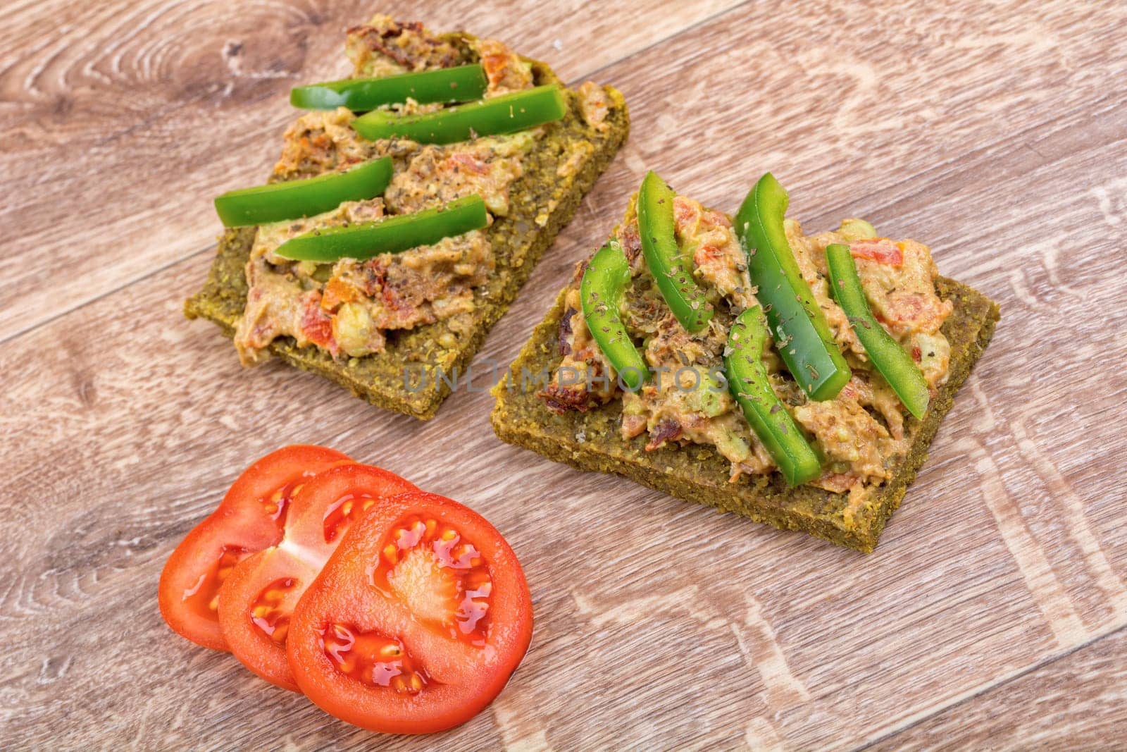 Raw bread with a spread decorated with green pepper and tomatoes