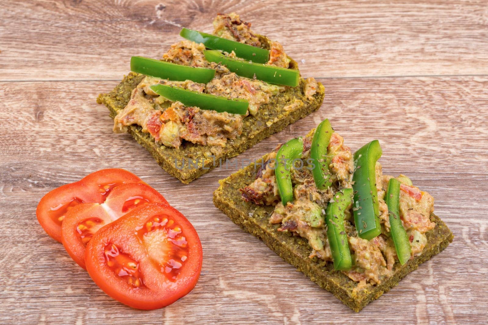 Raw bread with a spread decorated with green pepper and tomatoes