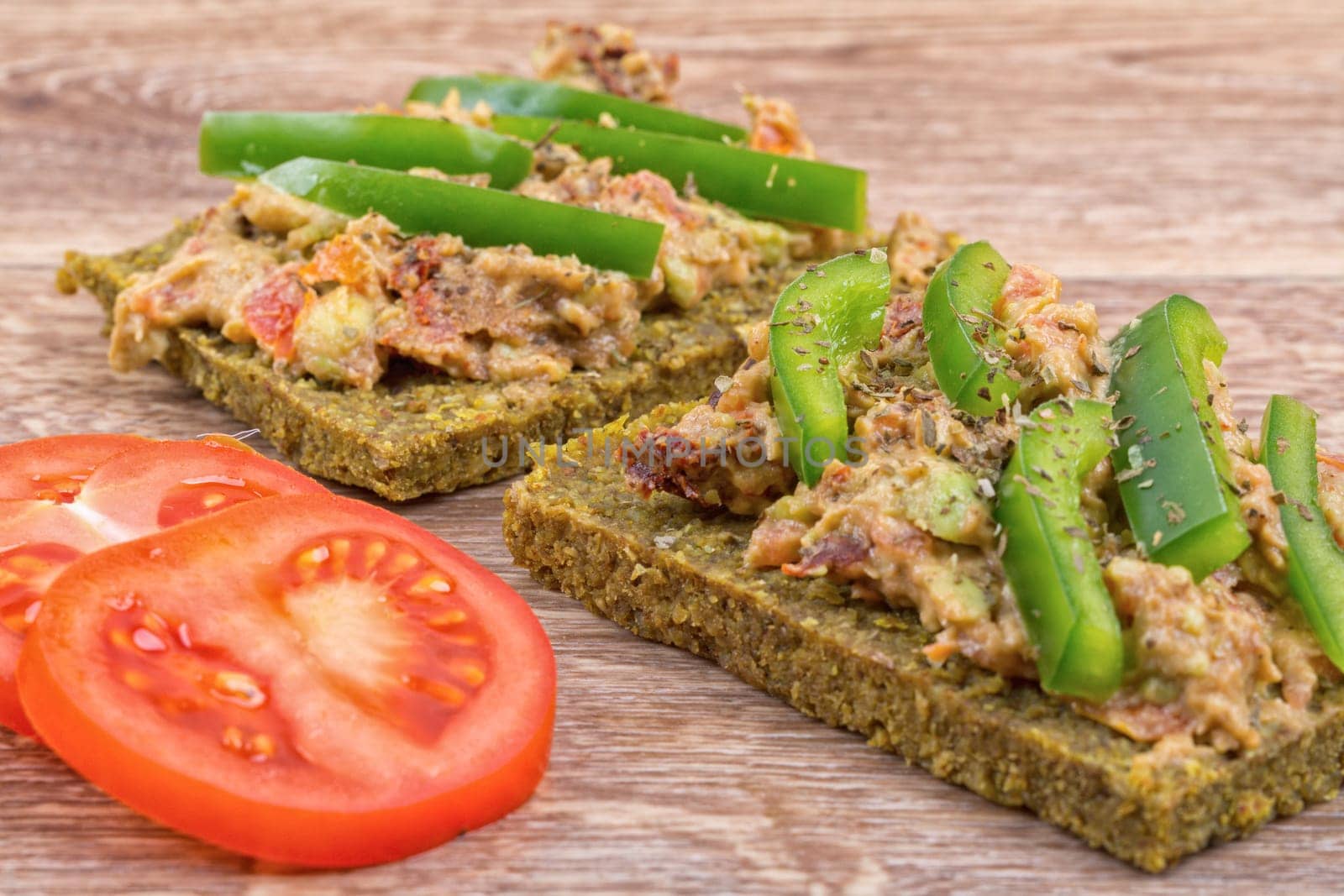 Raw bread with a spread decorated with green pepper and tomatoes