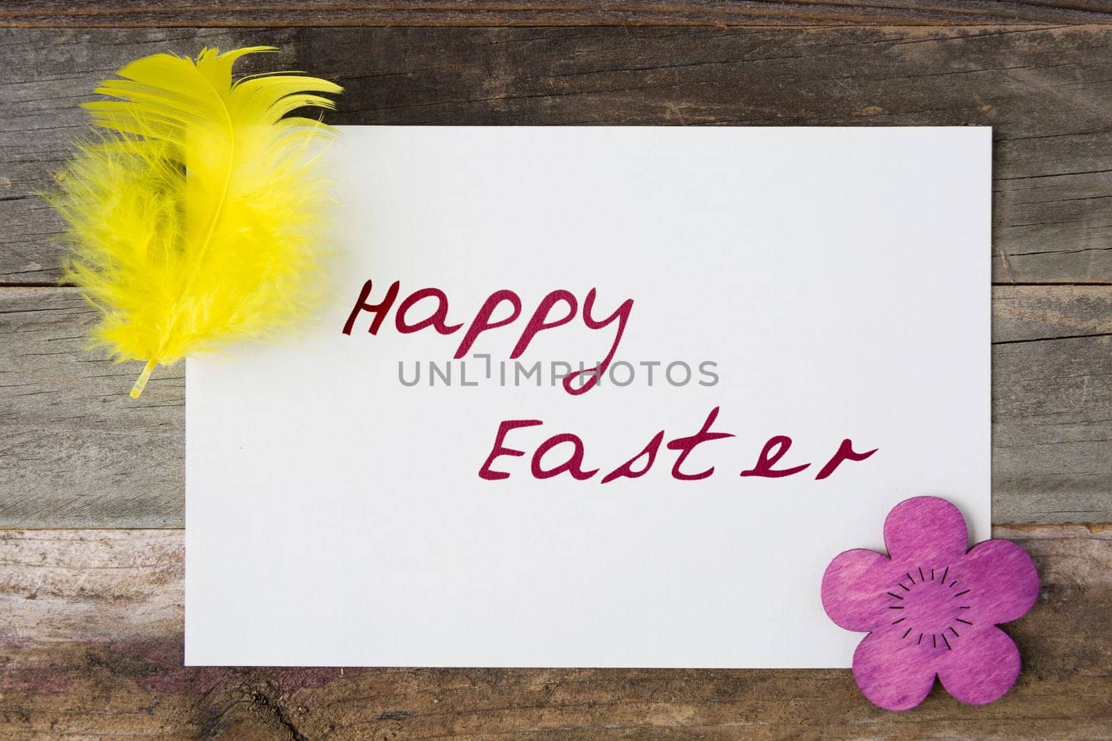 Happy Easter greeting card surrounded by feather and wooden Easter flower.