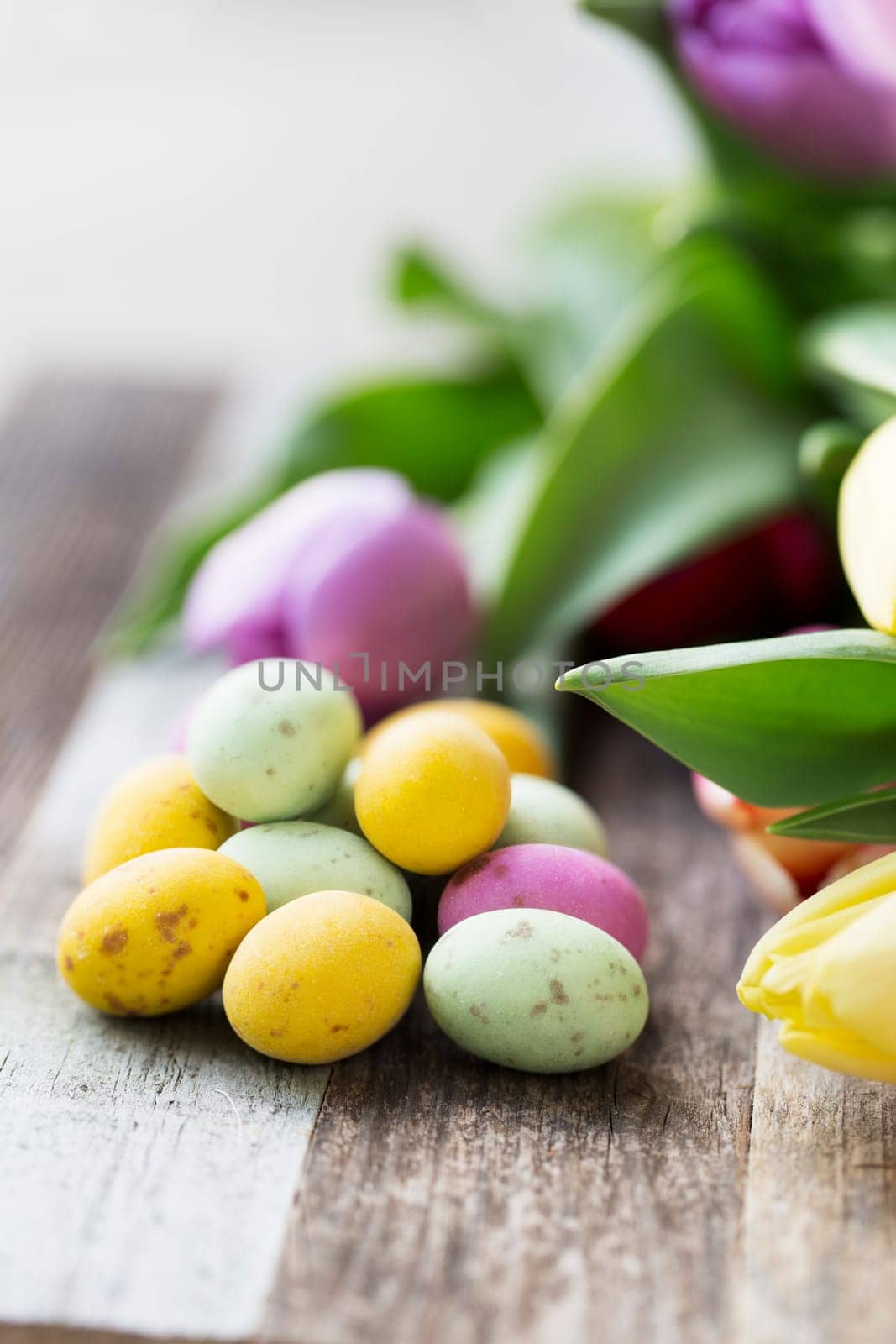 Close up of milk chocolate eggs on table with flowers vertical orientation.