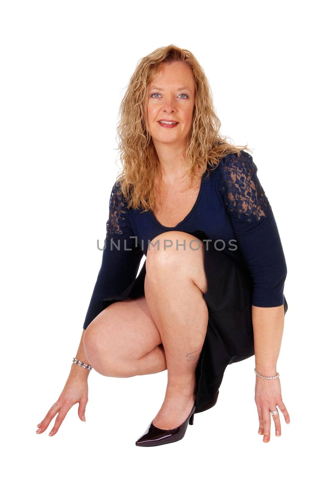 A beautiful blond woman crouching on the floor in a black skirt and navy.top, isolated for white background..