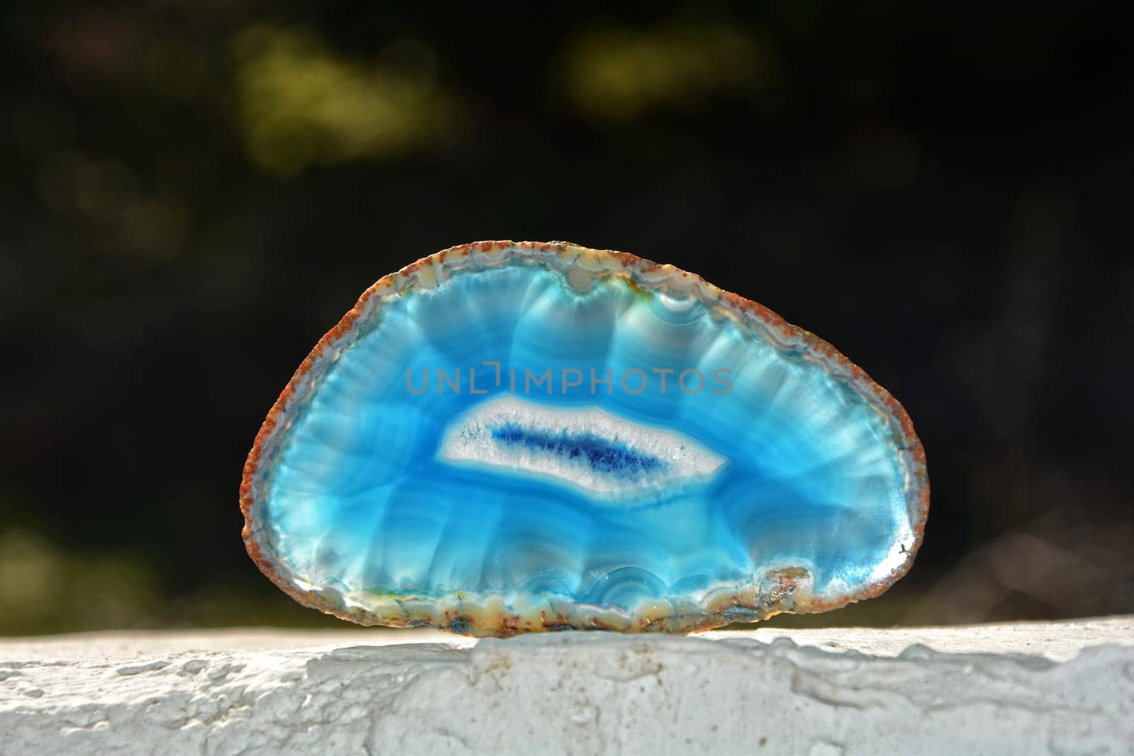 Light blue agate - disc on white wall with dark background and sunlight from behind