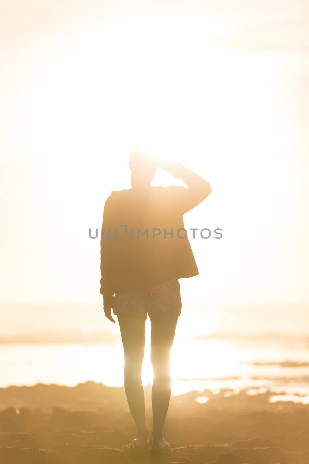 Silhouette of casualy dressed sporty woman watching sunset at the beach.