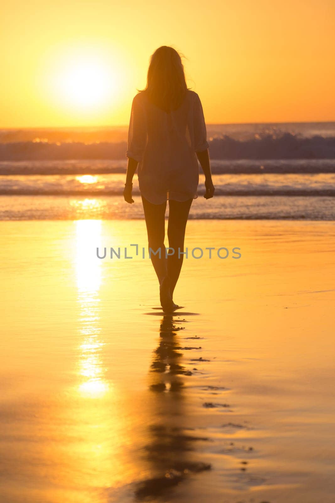 Woman walking on sandy beach in sunset leaving footprints in the sand. Beach, travel, concept. Copy space. Vertical composition.