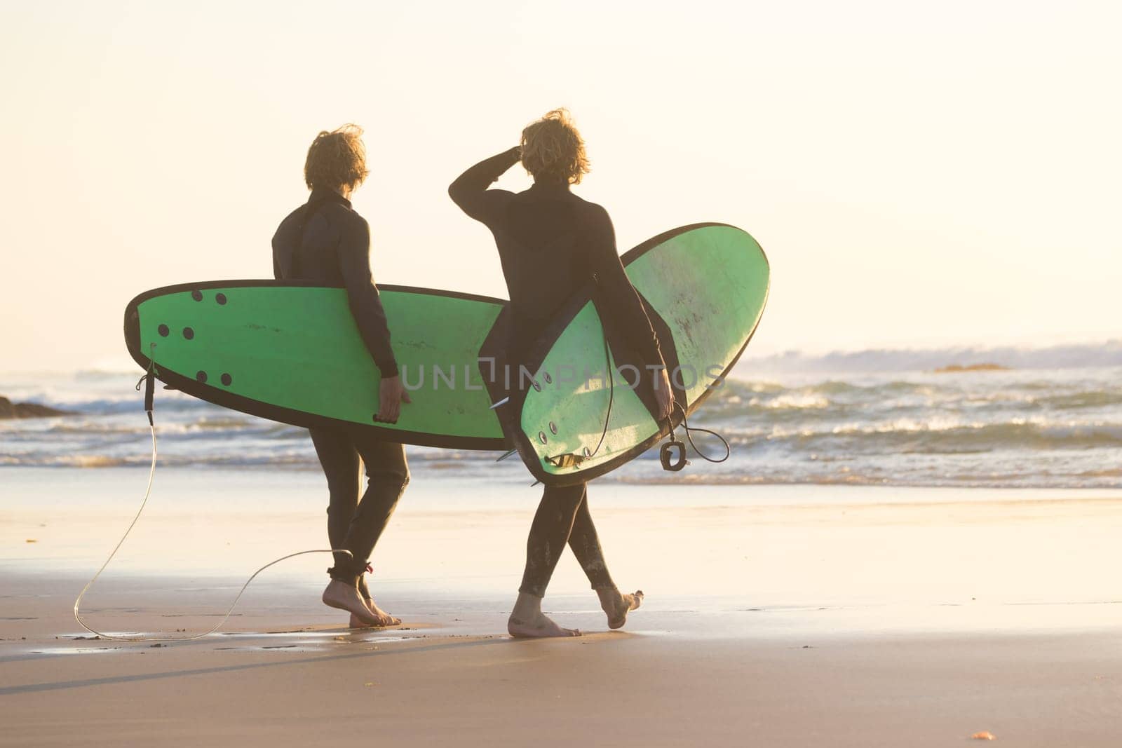 Male surfers on sandy beach with the surfboard in sunset.