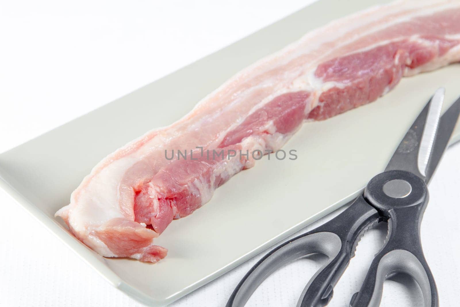 streaky pork with scissors in plate on white background