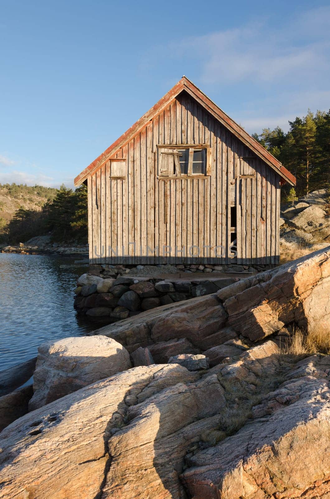 Old boathouse standing betwen the water on stone and in the sunshine
