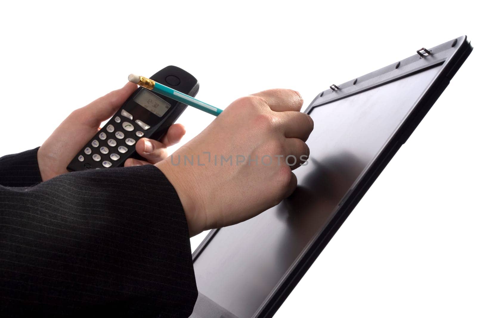 A businessman is writing notes in his agenda on a laptopscreen while holding a mobile phone.
