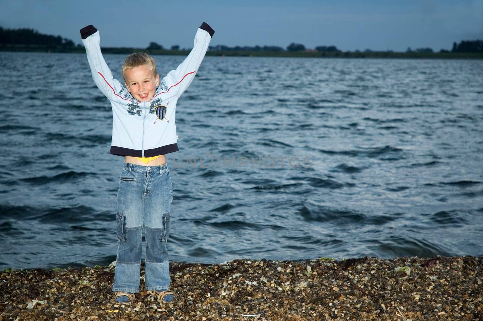 Boy standing in front of a lake at night, holding his hands in the sky.
