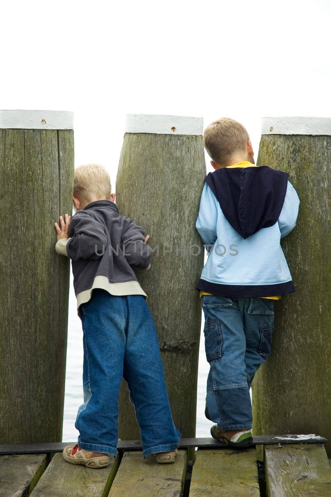 Two boys looking though a couple of poles, to see what's beyond. On white background.
